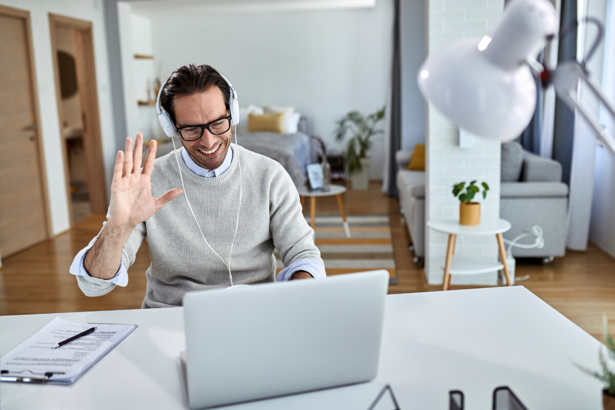 Young happy businessman waving while having online meeting over laptop from home.